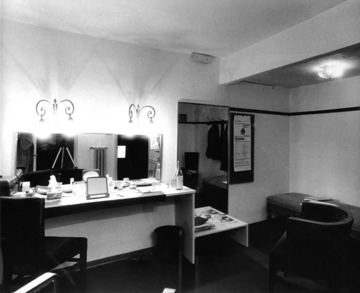 Interno del camerino di Eleonora Duse, con console davanti a uno specchio a parte, coperta di trucchi di scena. Due lampadari da parete illuminano la console. Sulla destra una poltroncina e un divanetto