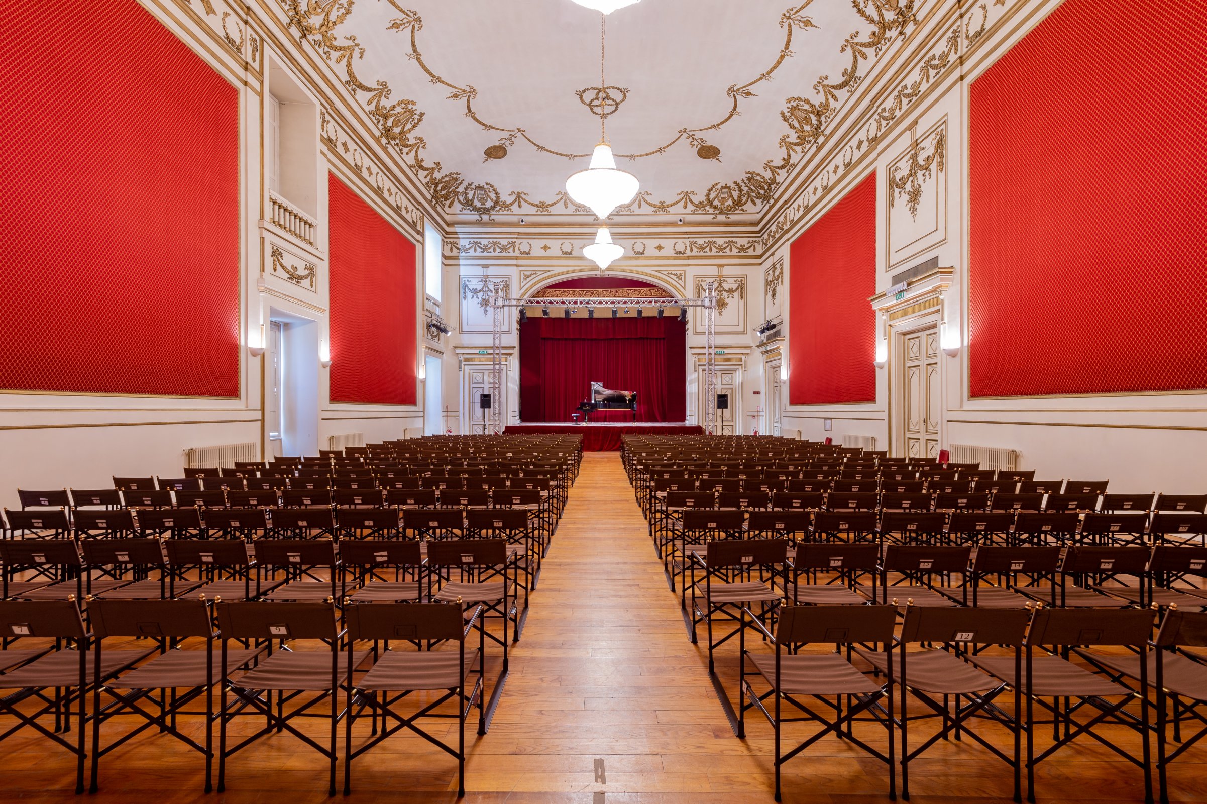 sala interna del teatro per concerti musicali con sedie come sedute e colori rossi accesi sulla parete